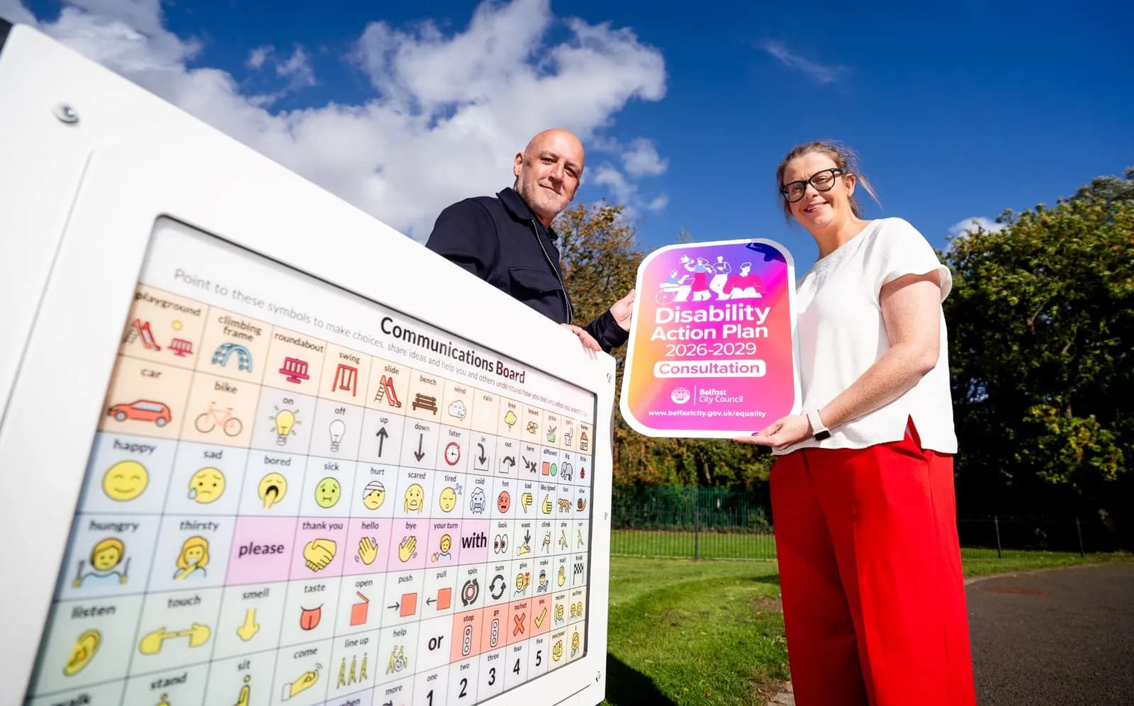 A man and a woman stand next to a communication board, with the woman holding a sign for a "Disability Action Plan 2026-2029 Consultation."