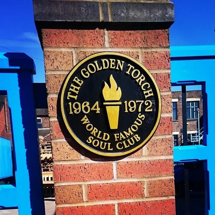 A round black and gold sign for "The Golden Torch: 1964-1972 World Famous Soul Club" is mounted on a brick pillar.