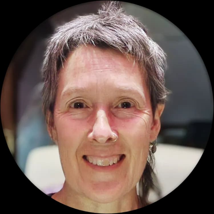 A smiling person with short gray hair and a nose ring looks directly at the viewer.