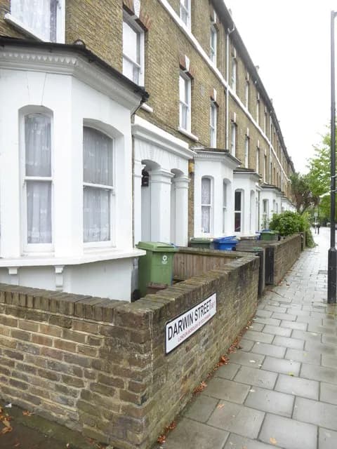 A row of London brick houses with white bay windows and a brick wall in the foreground with a 'Darwin Street' sign.