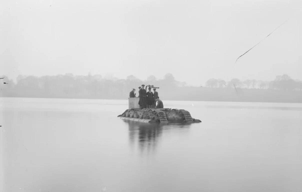 A group of six men in uniform stand aboard a makeshift floating platform resembling a tank in a vast body of water, with trees visible in the hazy distance.