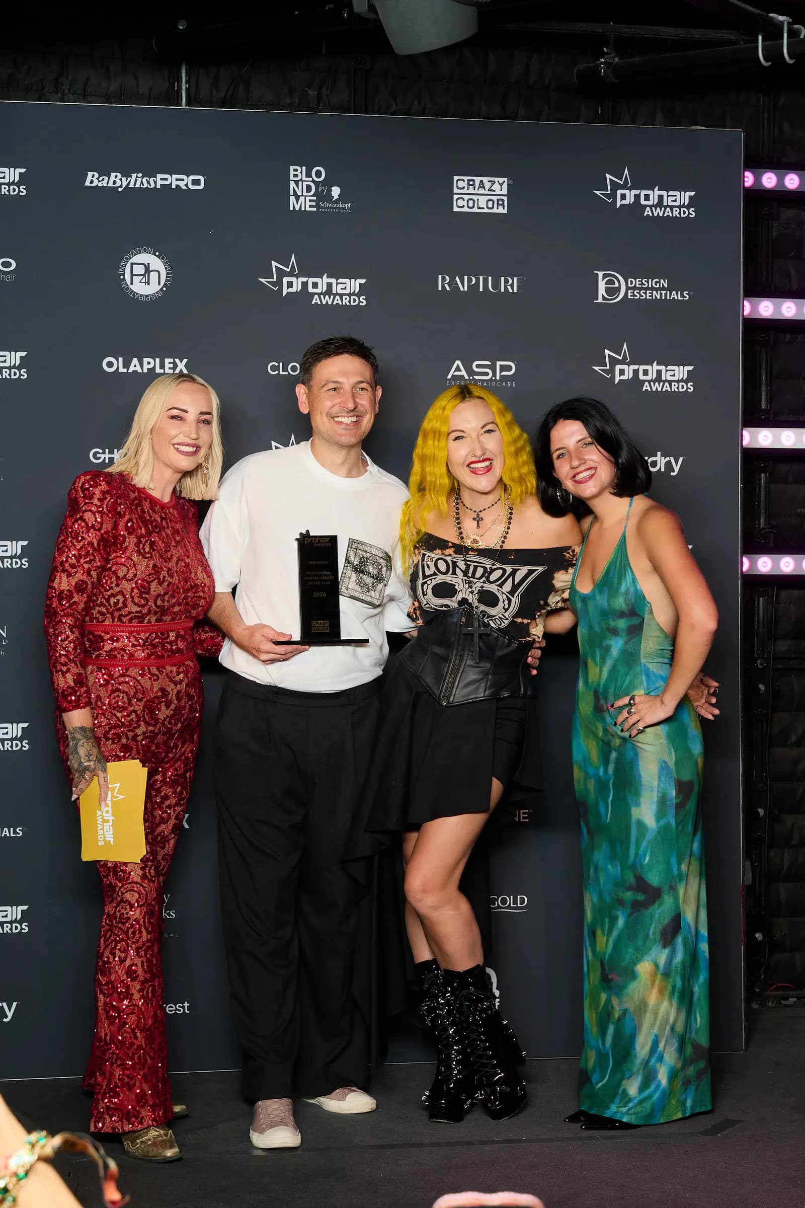 Four people, two women and two men, pose for a photo with an award in front of a black backdrop featuring various brand logos and the 'prohair AWARDS' logo.