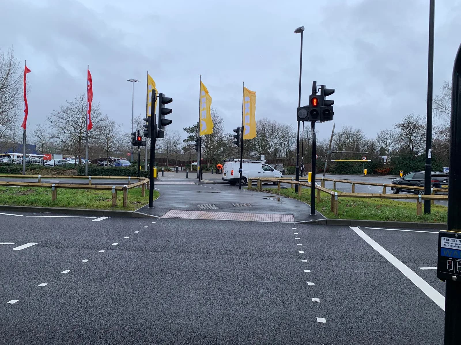 A view of a road intersection with pedestrian crossings and traffic lights, with several yellow flags and some red flags visible in the background, under a cloudy sky.