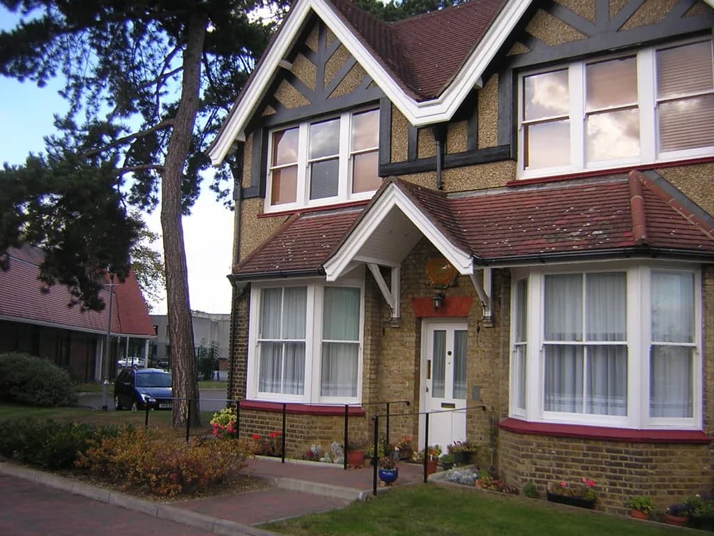 A large, two-story house with a brick ground floor, a textured upper floor, and a dark brown tiled roof, featuring multiple windows and a white front door.