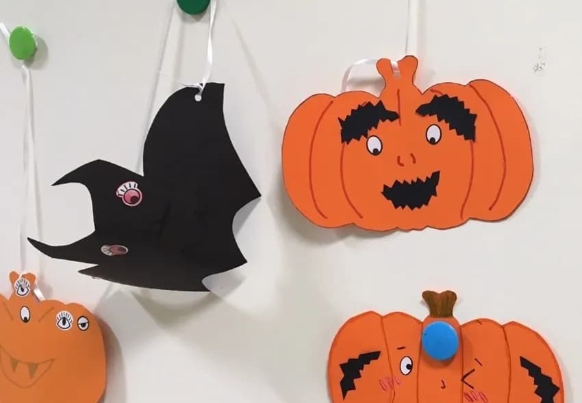 Halloween decorations including an orange pumpkin with a surprised expression and a black bat with a pink eye hanging against a white wall.