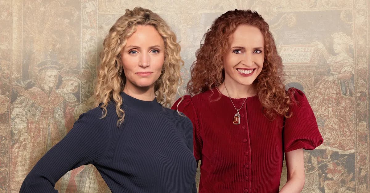 Two women with curly hair stand in front of a patterned backdrop, one with blonde hair looking forward and one with red hair smiling at the camera.