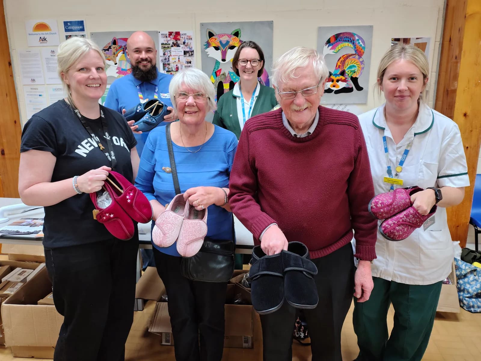 Six people in a room, some wearing medical scrubs, holding various pairs of slippers.