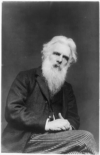 A black and white image capturing the bust of a serious-looking man with a long, flowing white beard and hair.