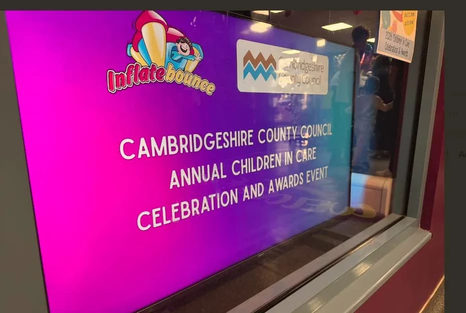 A magenta and blue sign advertises the Cambridgeshire County Council Annual Children in Care Celebration and Awards Event.