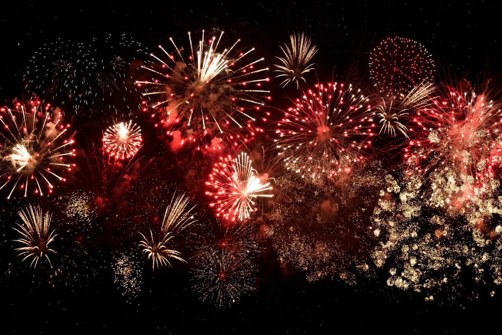 Red and gold fireworks explode across a dark night sky, illuminating the scene with brilliant light.