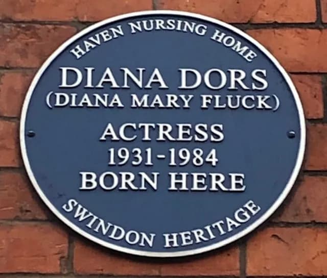 A blue circular plaque with white text on a brick wall, commemorating Diana Dors (Diana Mary Fluck), Actress 1931-1984, stating she was born here, with top text "HAVEN NURSING HOME" and bottom text "SWINDON HERITAGE".