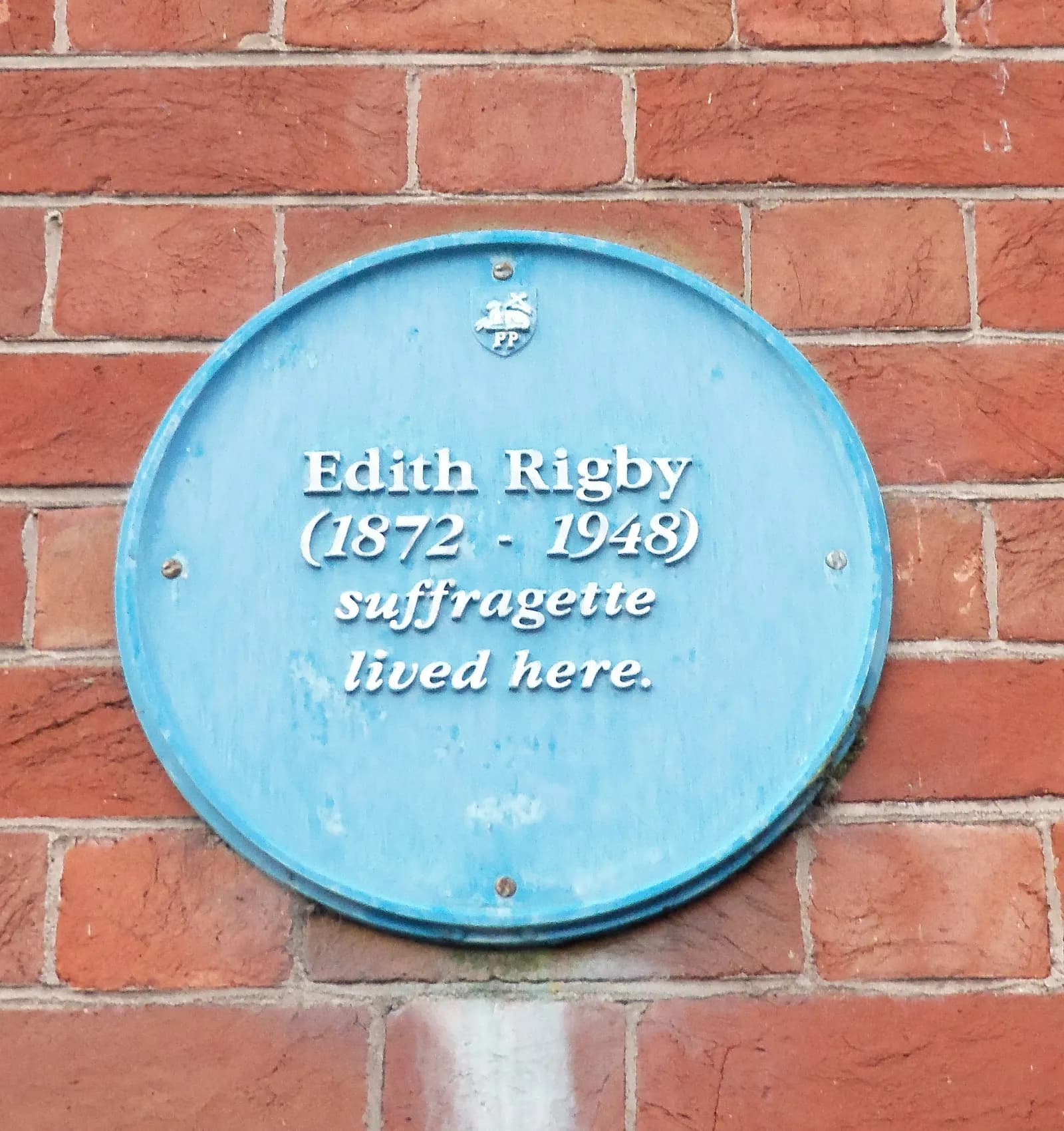 A light blue circular plaque on a brick wall, stating "Edith Rigby (1872 - 1948) suffragette lived here."