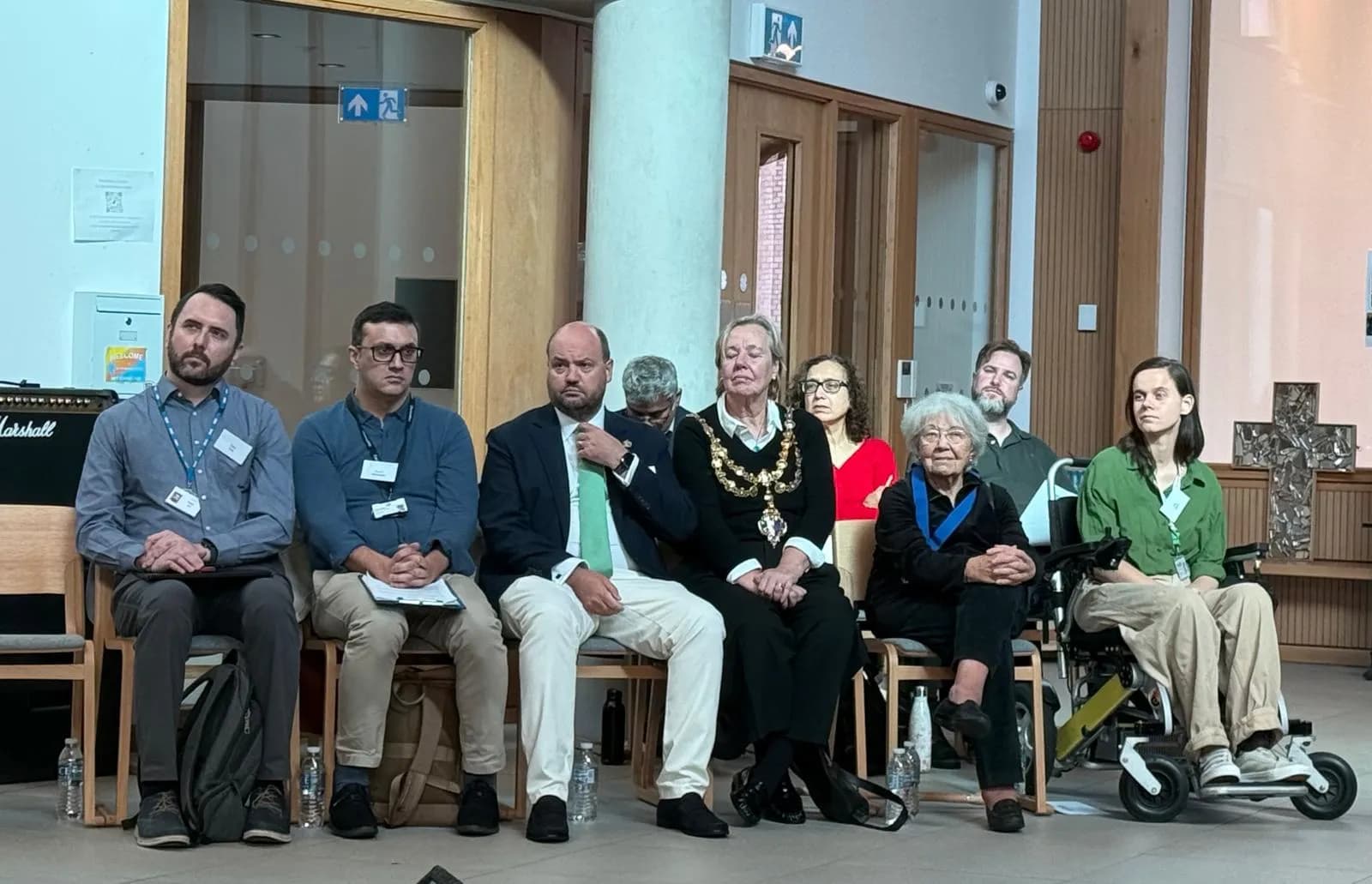A diverse group of people, including men, women, and individuals using mobility aids, are seated in a row, attentive during an event.