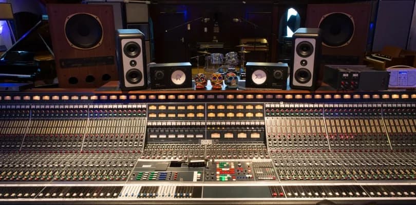 A professional recording studio control room featuring a large sound mixing console with many sliders and knobs, flanked by various studio monitors and decorated with three skull figures.
