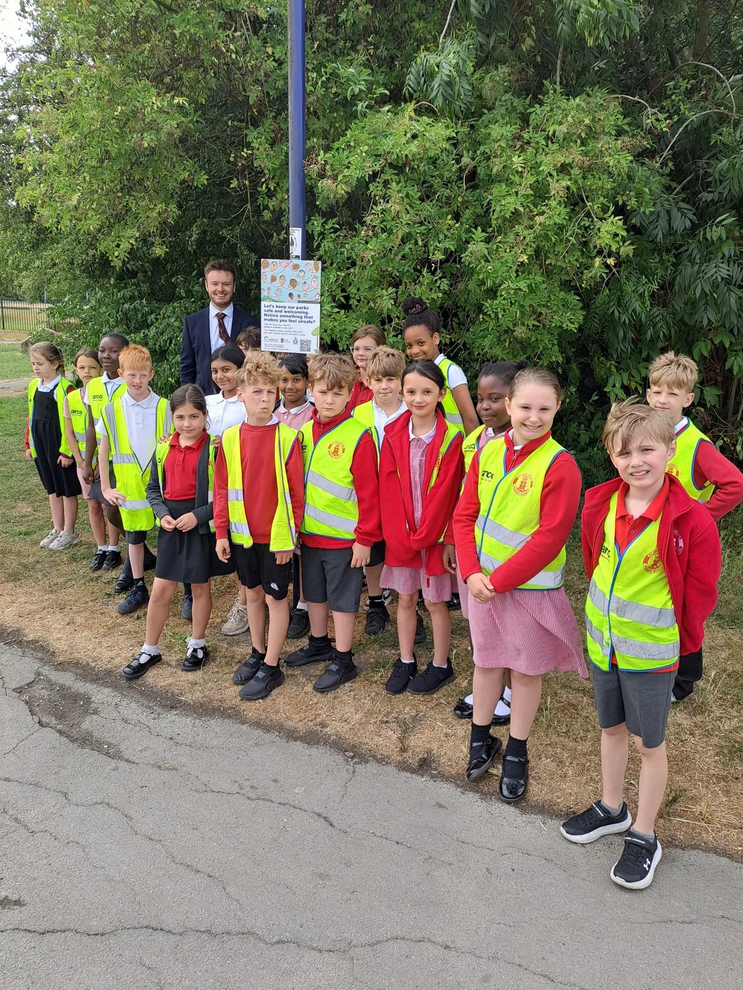 A man in a suit posing with a group of young children wearing high-visibility vests.