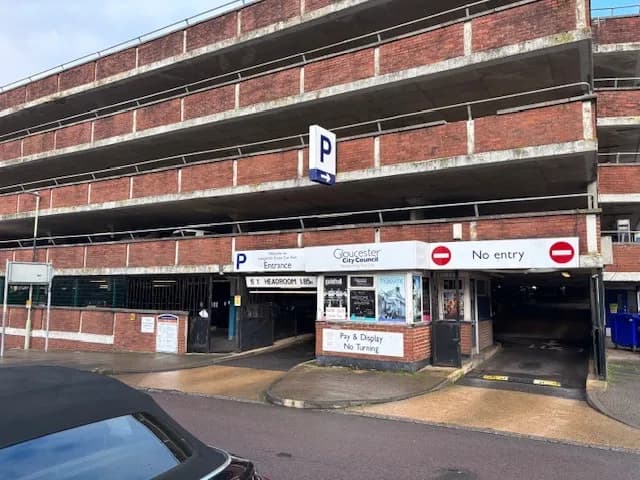 A multi-story brick parking garage with an entrance and exit, complete with signs for 'Gloucester City Council' and 'No entry' above the entry lanes.
