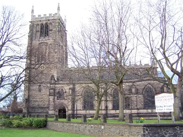 A large stone church with a tall, ornate tower on the left, mostly obscured by bare trees with green grass in the foreground.