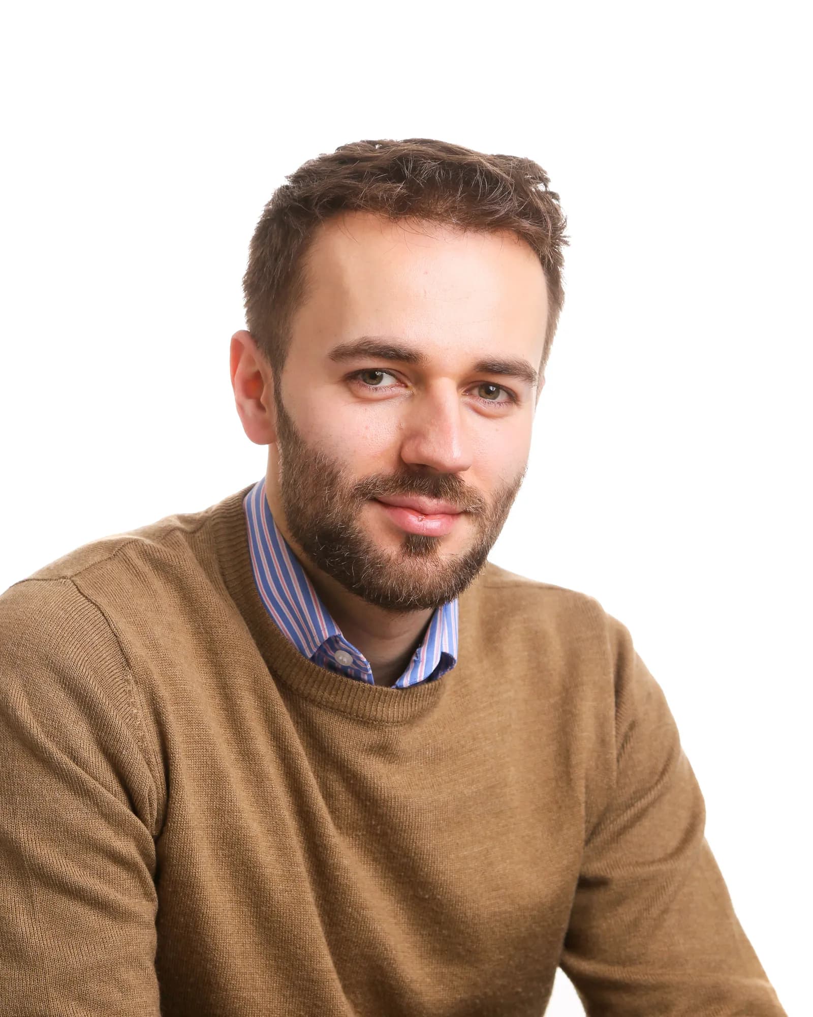 A man with a beard and brown hair, wearing a brown sweater over a blue and white striped shirt, looks directly at the viewer.
