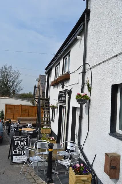 An outdoor seating area with chairs and tables in front of a white building with black accents and a "Traditional Fish & Chip" sign.