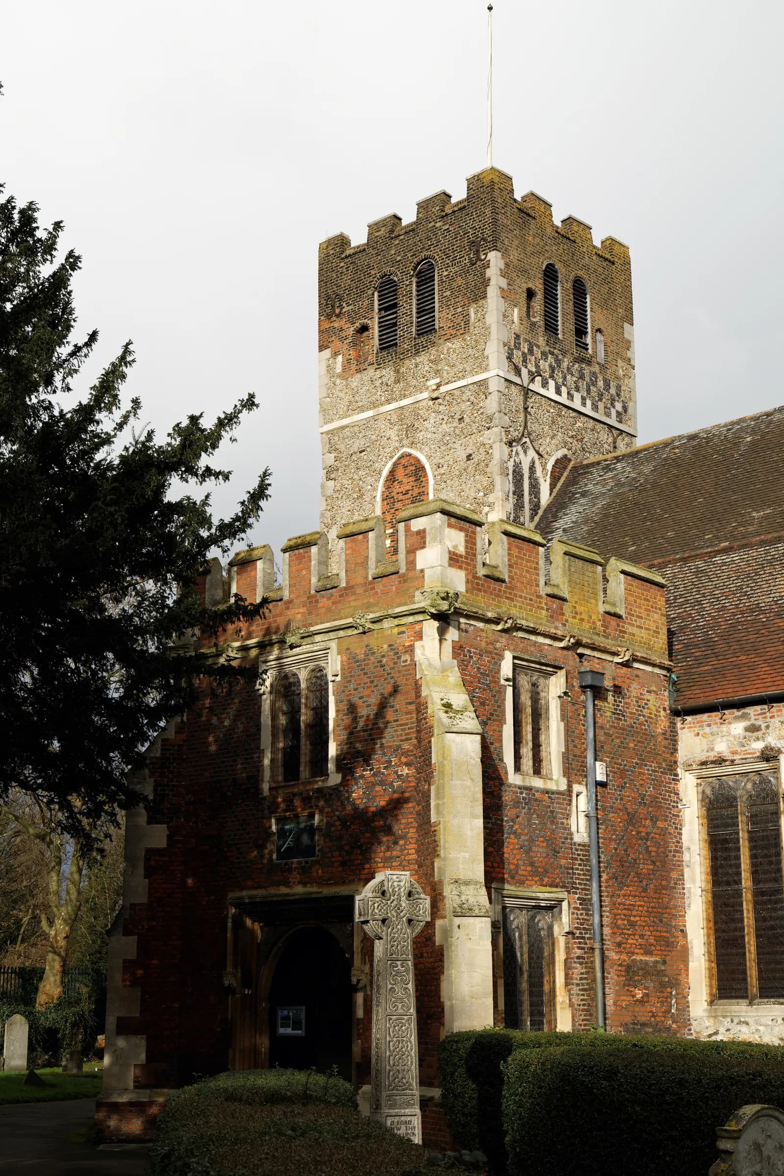 A historic church with a multi-level tower made of brick and stone, featuring arched windows and crenellated battlements.