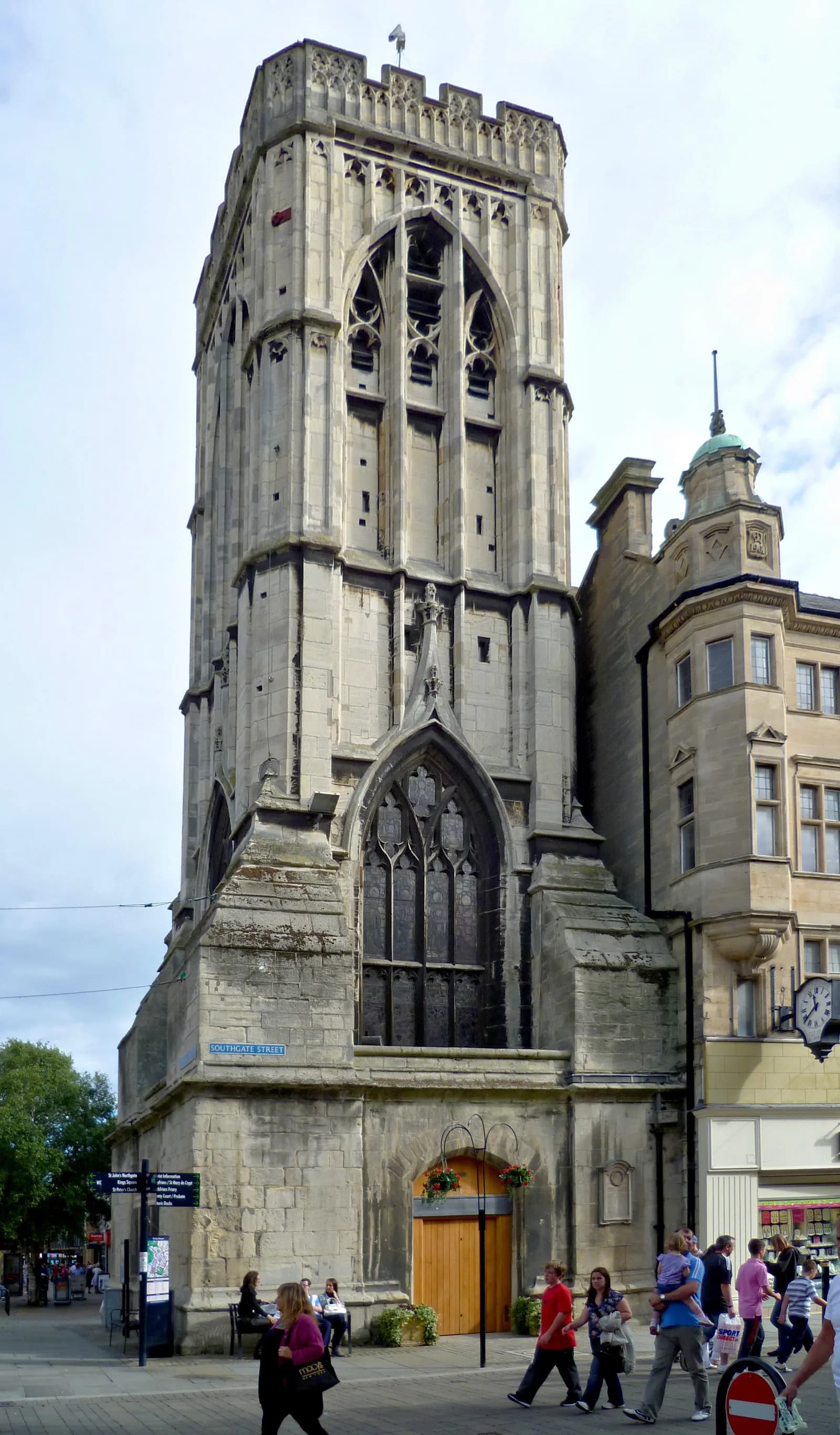 The Church of St Owen's tower with its large arched window dominates the left side of the frame, with a street full of pedestrians in the foreground.