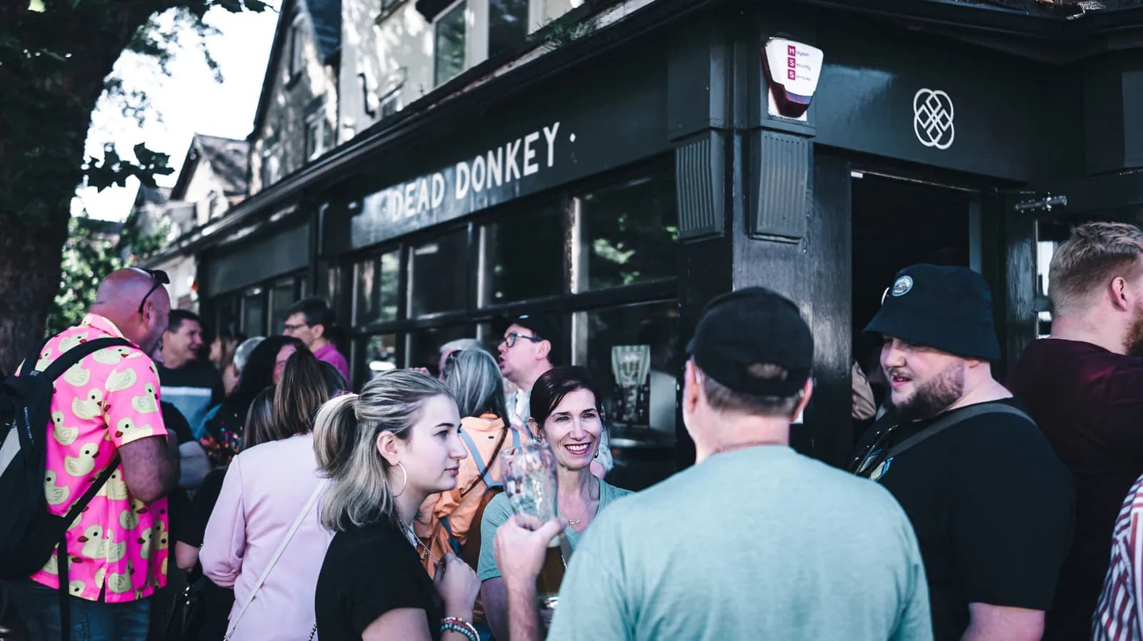 A group of people standing outside a pub that has "DEAD DONKEY" written on its facade.