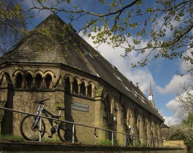 A large stone church building with an octagon-shaped front and a steep, dark tiled roof, with a bicycle parked against a railing in the foreground.