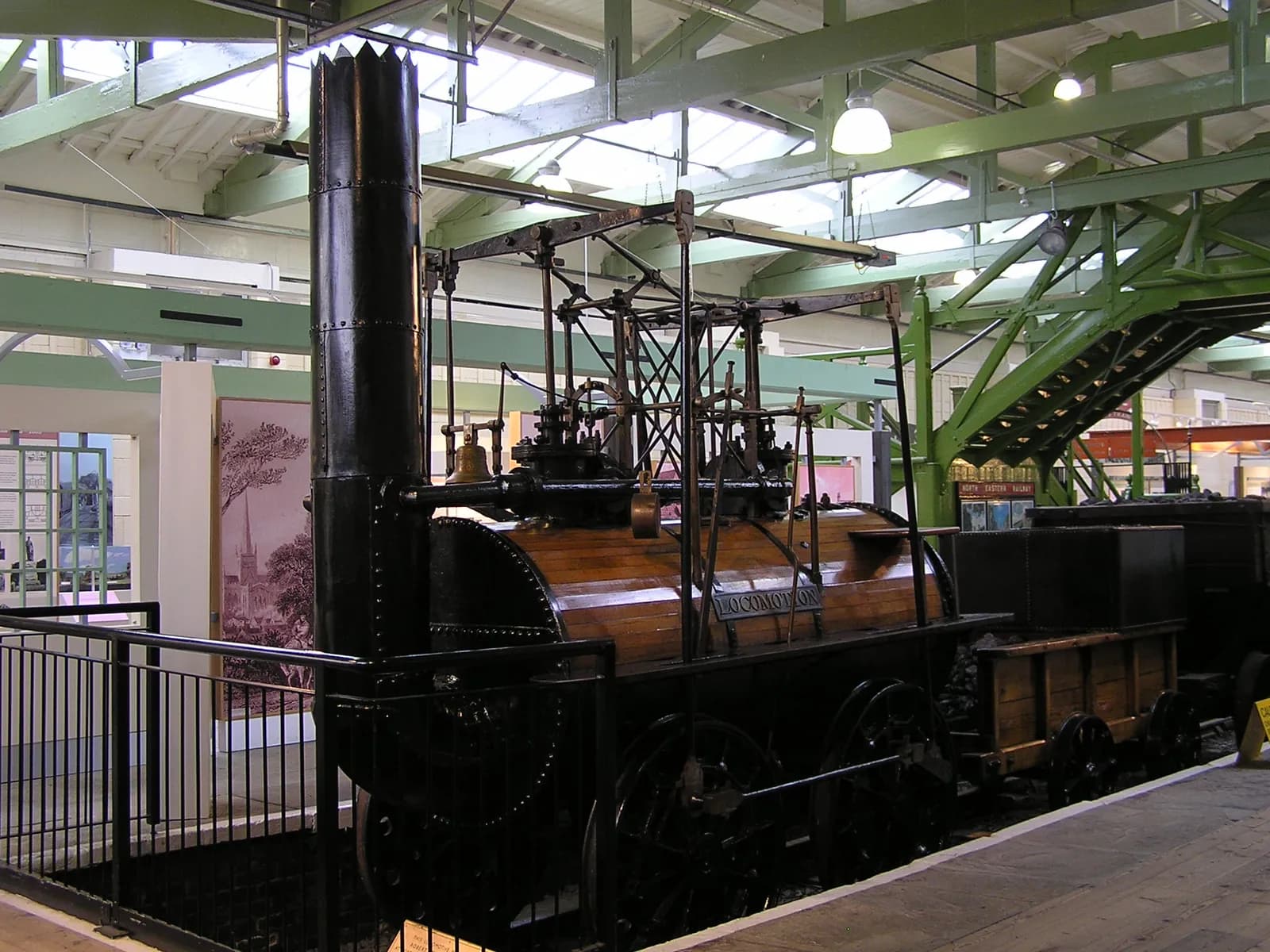 A historic steam locomotive with a tall black smokestack and a wooden body is on display in a museum setting.