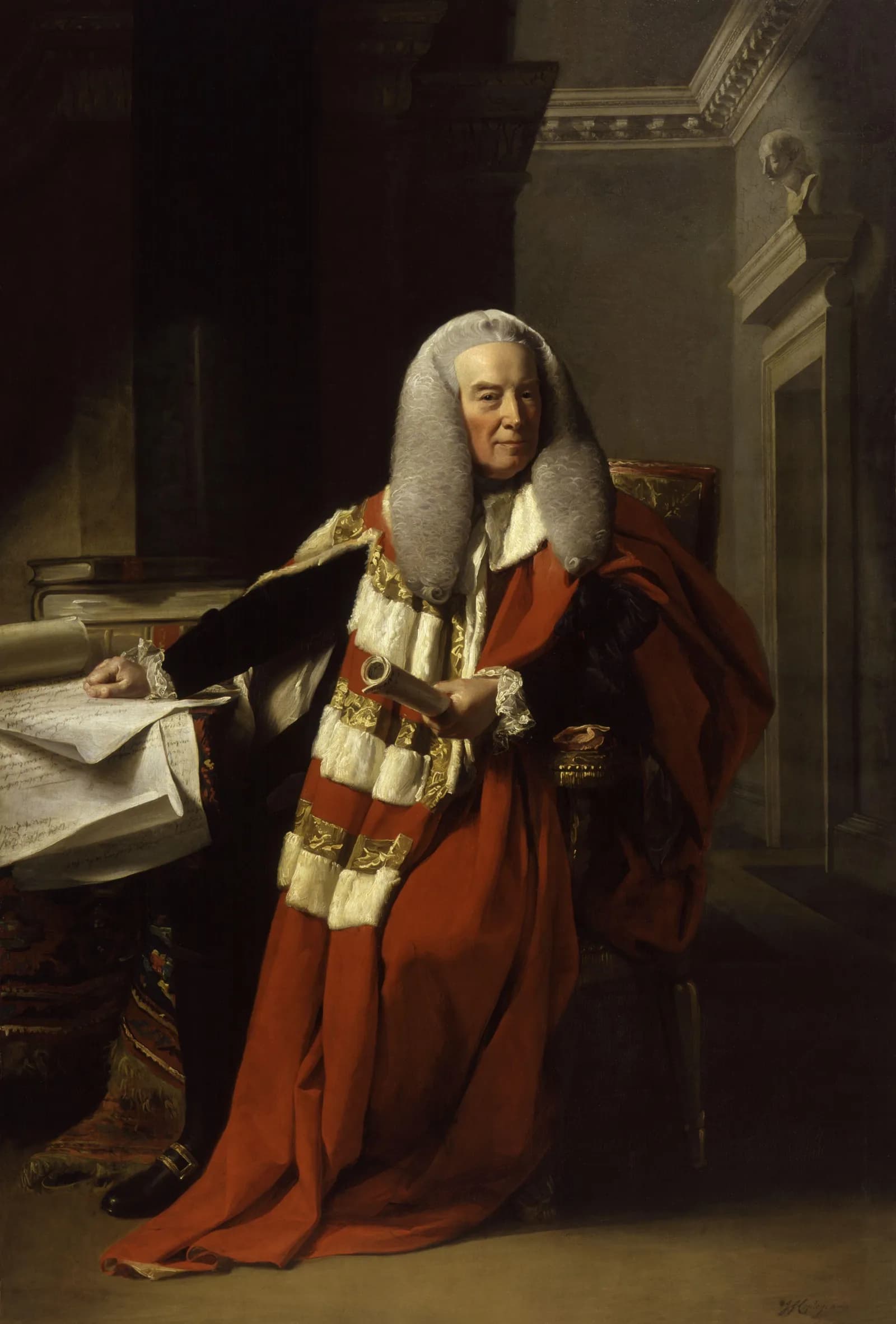 A man in a judge's wig and red robes sits at a desk, looking directly at the viewer.