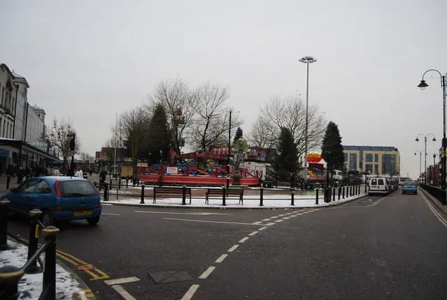 A fairground carousel, trees and people on a grey winter day.