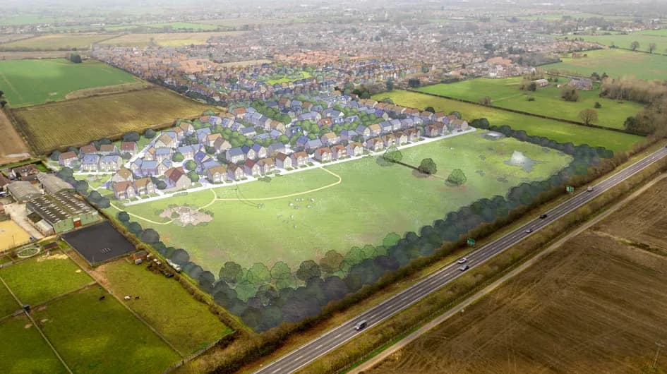 An aerial view shows a proposed housing development with many new homes clustered together next to a large green field and a highway, surrounded by existing rural landscape.