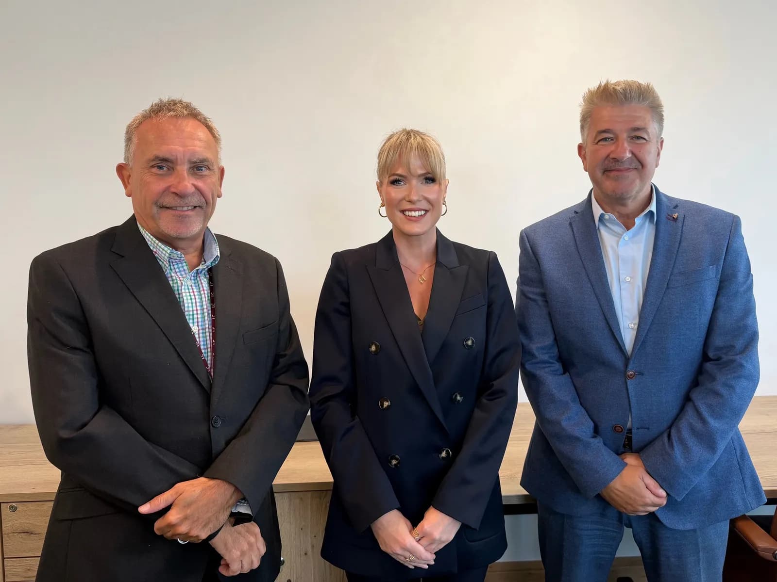 Three people, two men and one woman, stand side-by-side in business casual attire, smiling for a photo.