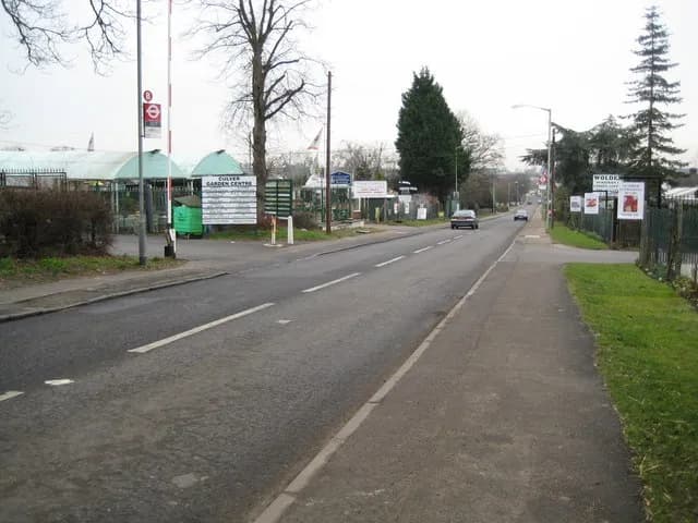 A long paved road leads into the distance with a green sign on the left for "Culver Garden Centre" and several signs for "Wolden Hall" on the right.