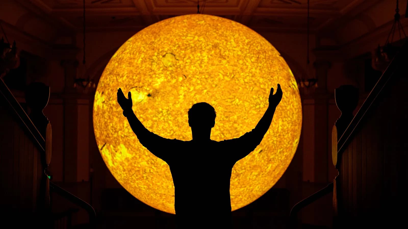 A silhouetted person with arms raised in front of a large, glowing orange sphere that resembles the sun.