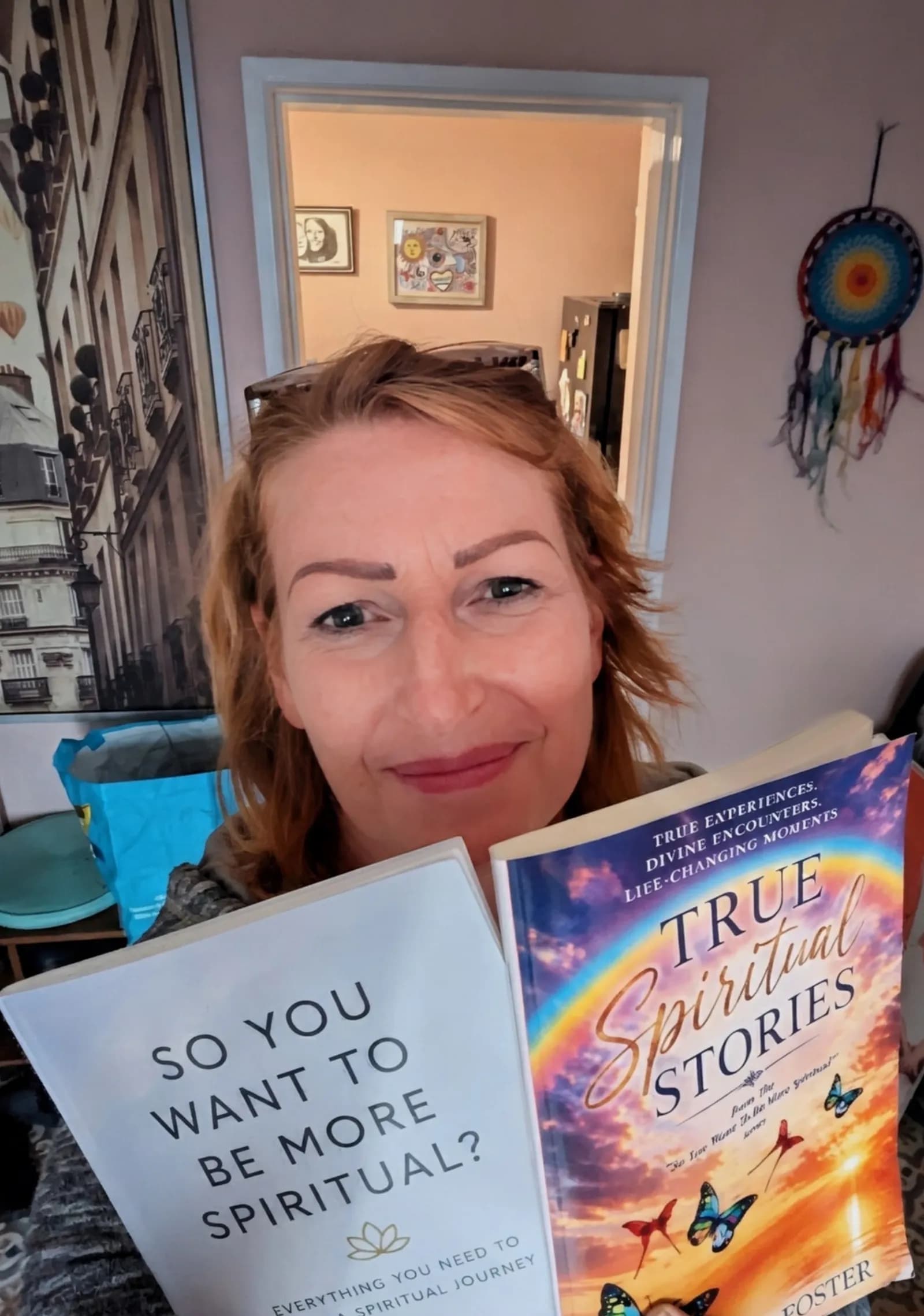 A smiling woman with reddish-brown hair holds two books titled 'So You Want to Be More Spiritual?' and 'True Spiritual Stories' in front of her.