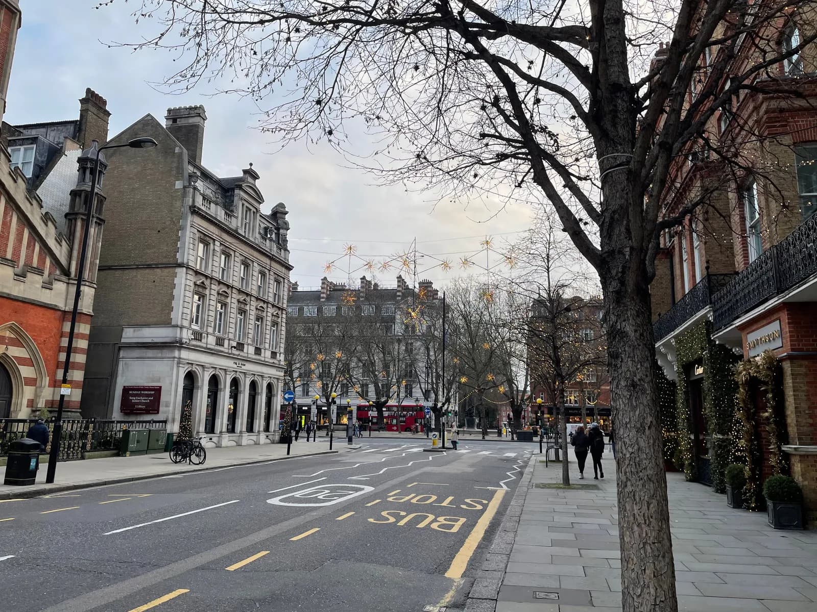 A street scene featuring ornate buildings, bare trees, and street decorations under a cloudy sky.
