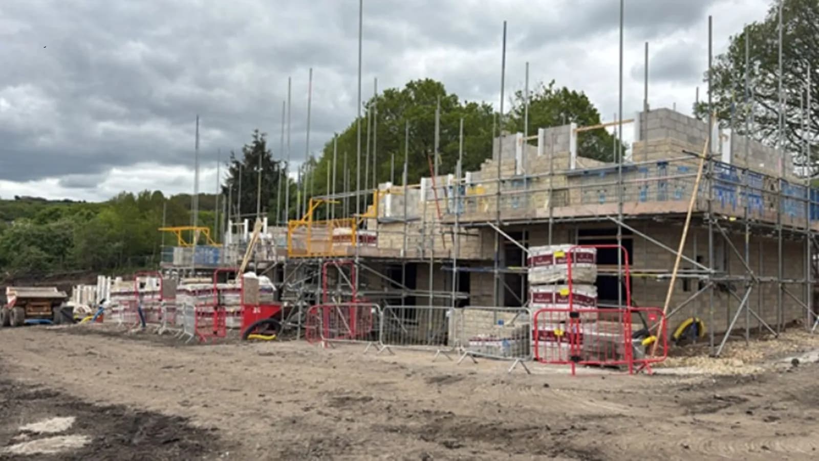 A new building under construction, surrounded by scaffolding and building materials, on a cloudy day.