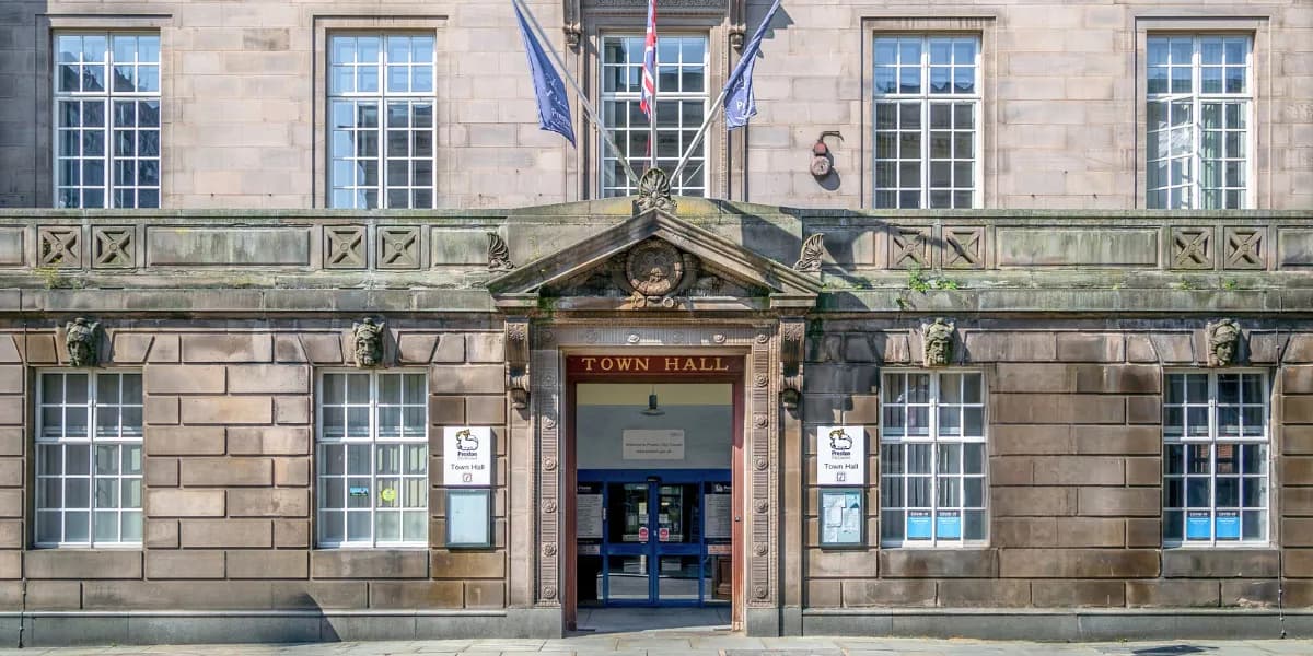 The entrance to Town Hall, a building made of light brown stone with many windows, and flags hanging above the doorway.