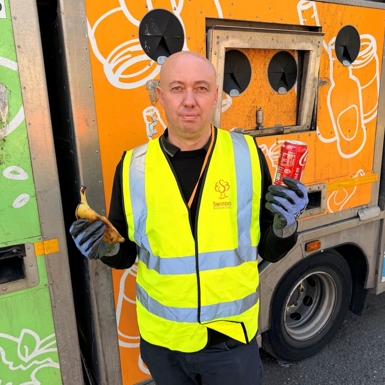 A man in a bright yellow reflective vest holds a banana peel in one hand and a Coca-Cola can in the other, standing in front of an orange recycling truck.