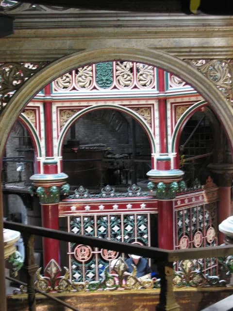 Ornate archways and railings inside a building with a multi-level structure visible in the background, featuring intricate designs in red, green, and gold.