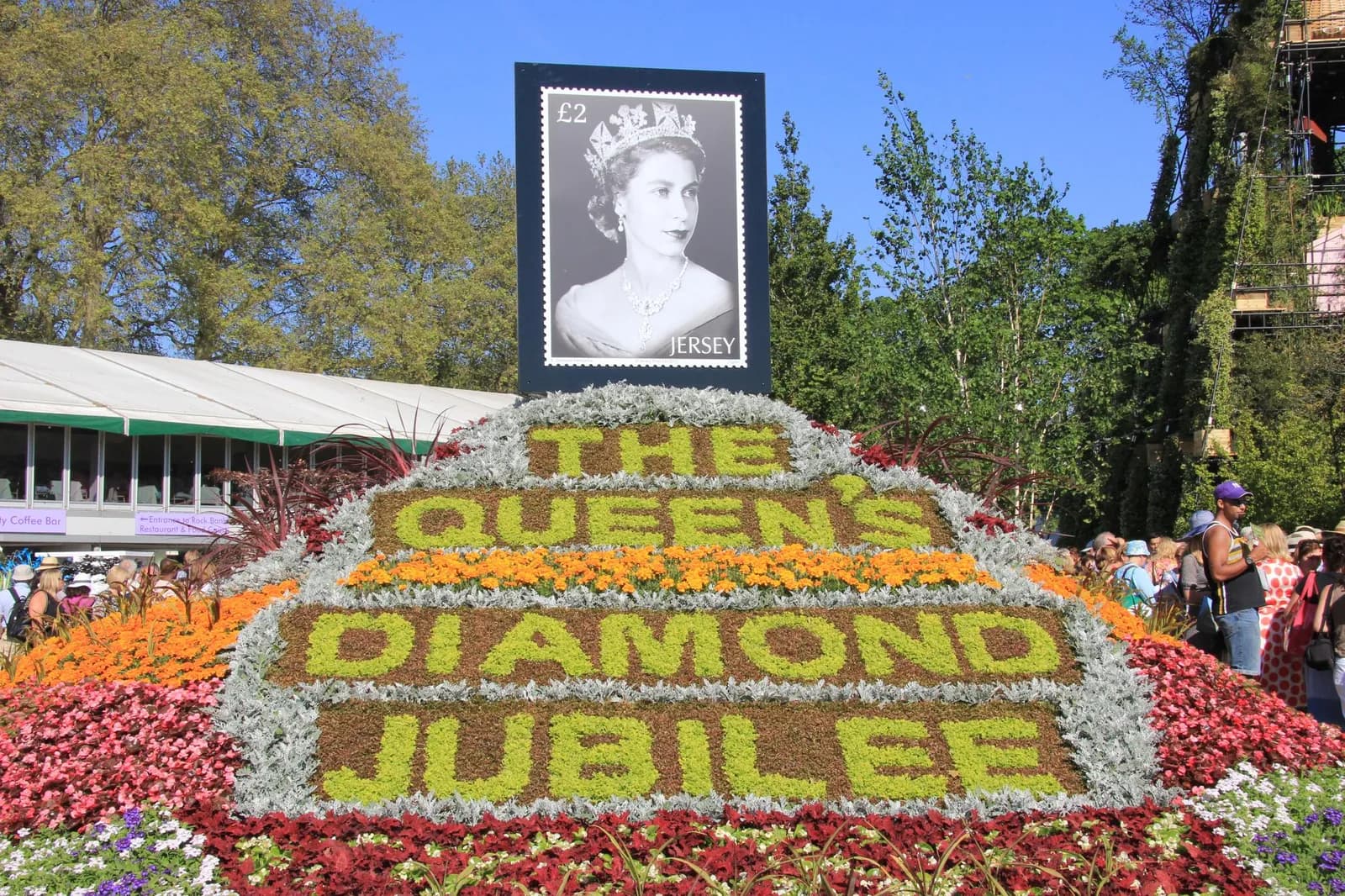 A floral display spelling out 'The Queen's Diamond Jubilee' in various colors, topped with a large black and white image of Queen Elizabeth II from a stamp.