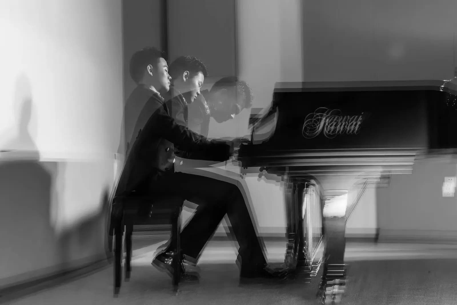 A grayscale photo of a person playing a Kawai grand piano, with a blurred motion effect suggesting movement and time passing.
