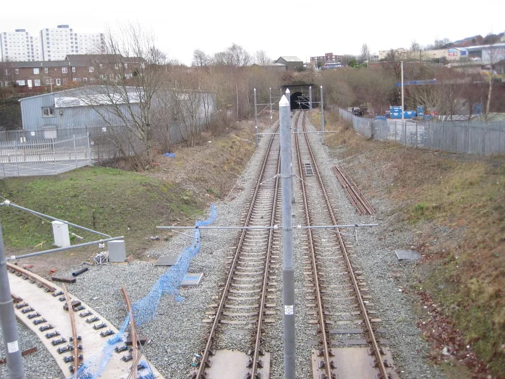 A wide shot shows a train track leading off into a dark tunnel and buildings in the background.